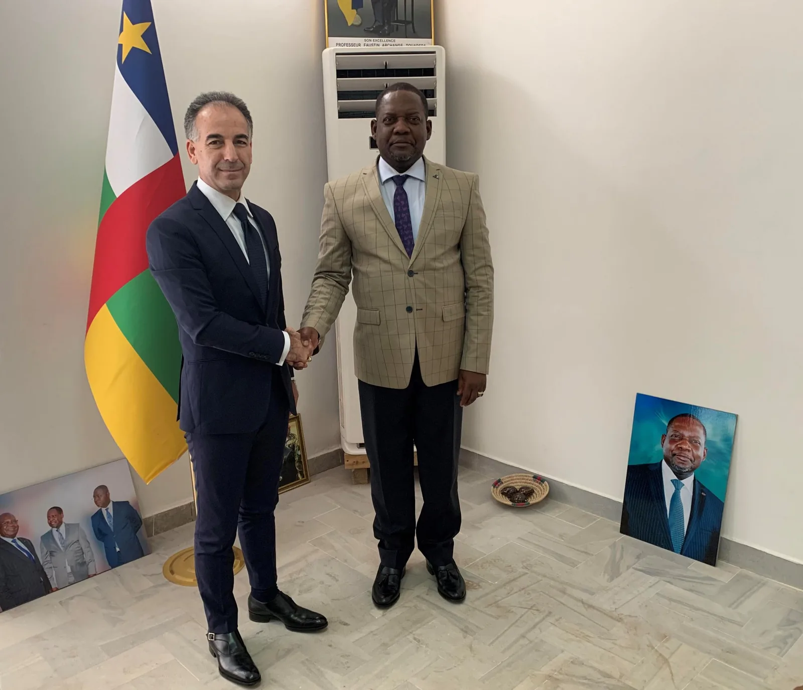 Şakir Yavuz i Sa Excel·lència Firmin Ngrebada donant-se la mà davant la bandera de la República Centreafricana